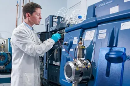 Research Technical Professional standing beside Mass Spectrometer